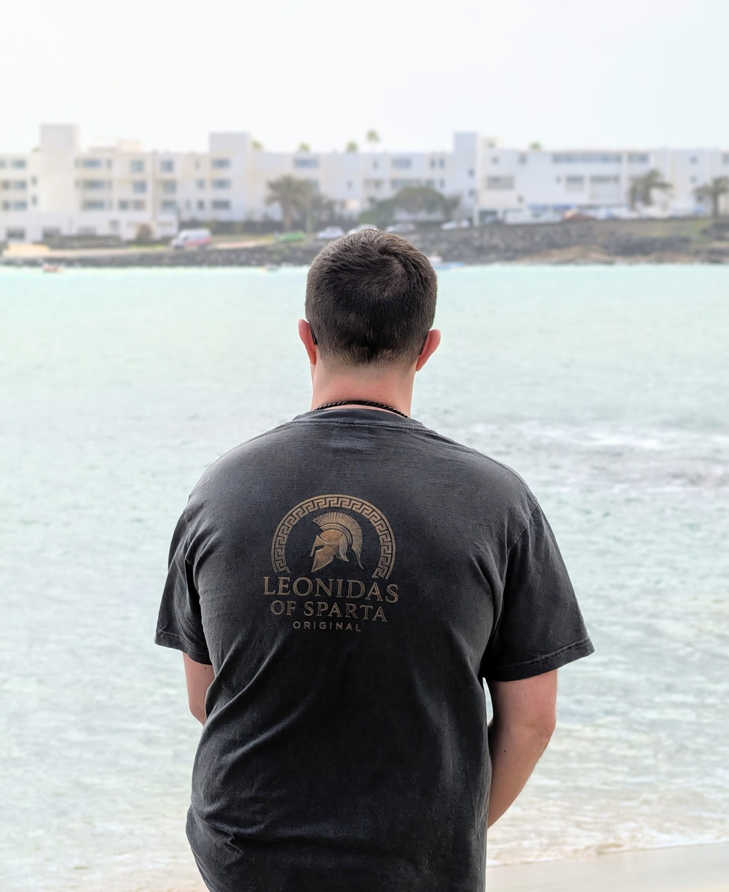 Person wearing a black t-shirt with 'Leonidas of Sparta' logo overlooking a body of water.