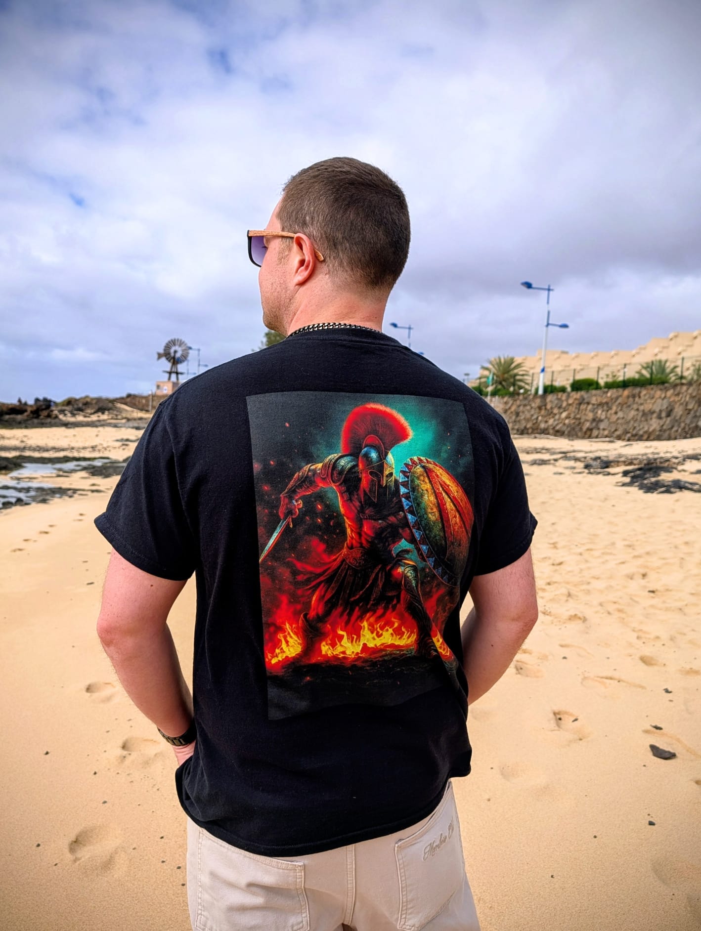 Man wearing a black t-shirt with a colorful graphic of Leonidas of Sparta on the beach