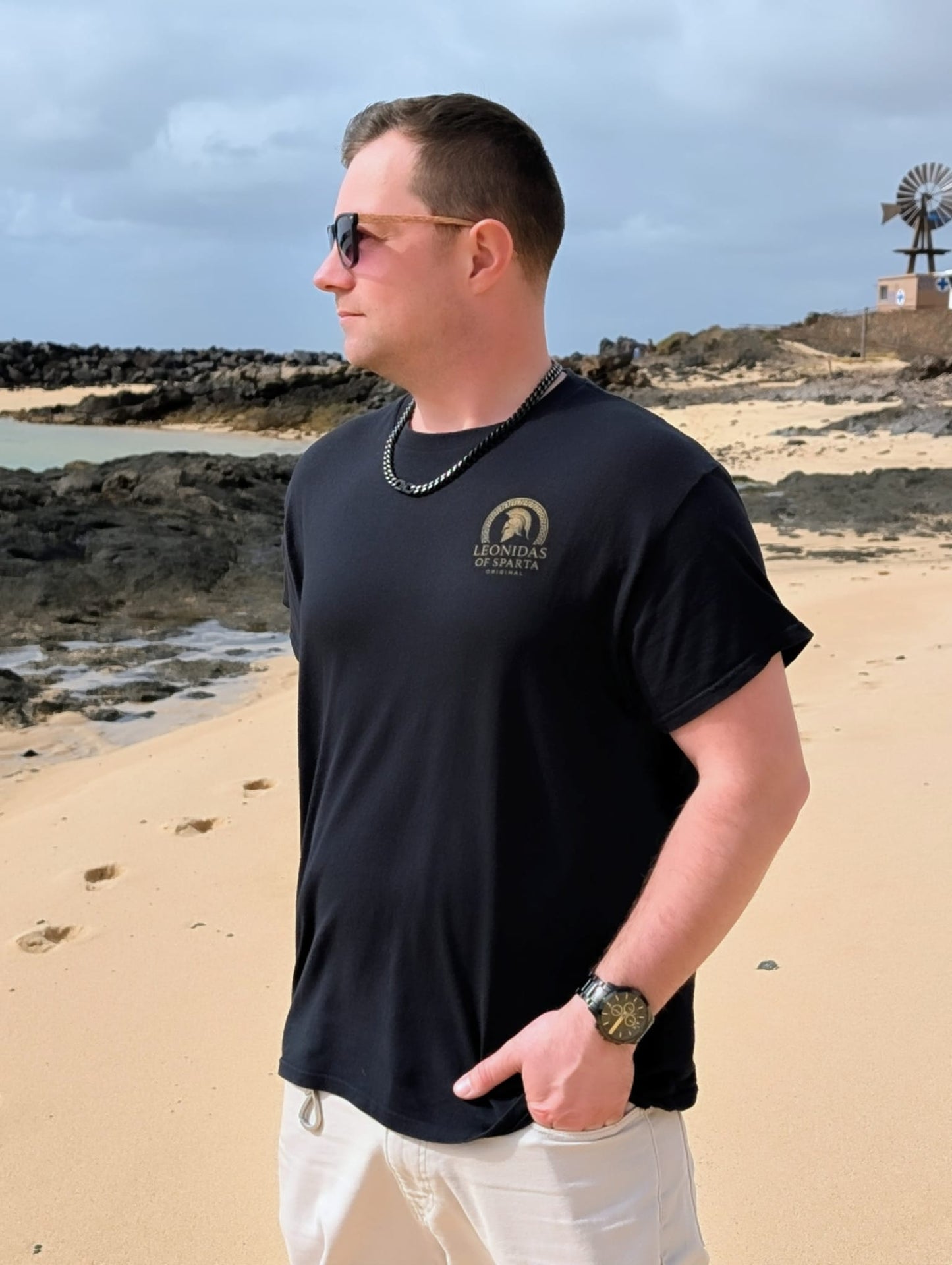 Man wearing a black t-shirt with Leonidas of Sparta Original logo on a beach