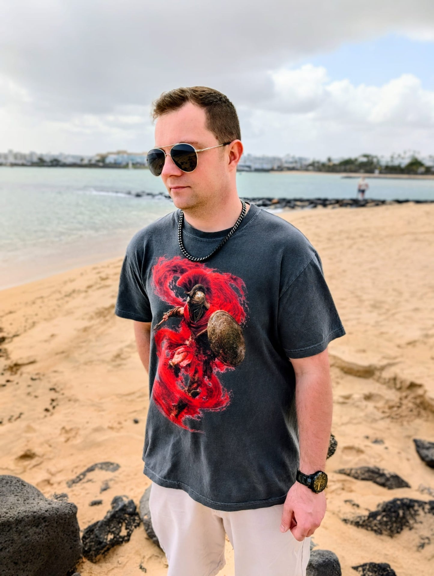 Man wearing a dark t-shirt with a red Leonidas of Sparta Original graphic design on a beach